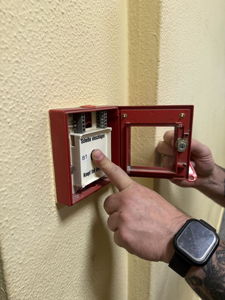 Prüfung eines geöffneten roten Handfeuermelders: Eine Person betätigt den Auslöseknopf.