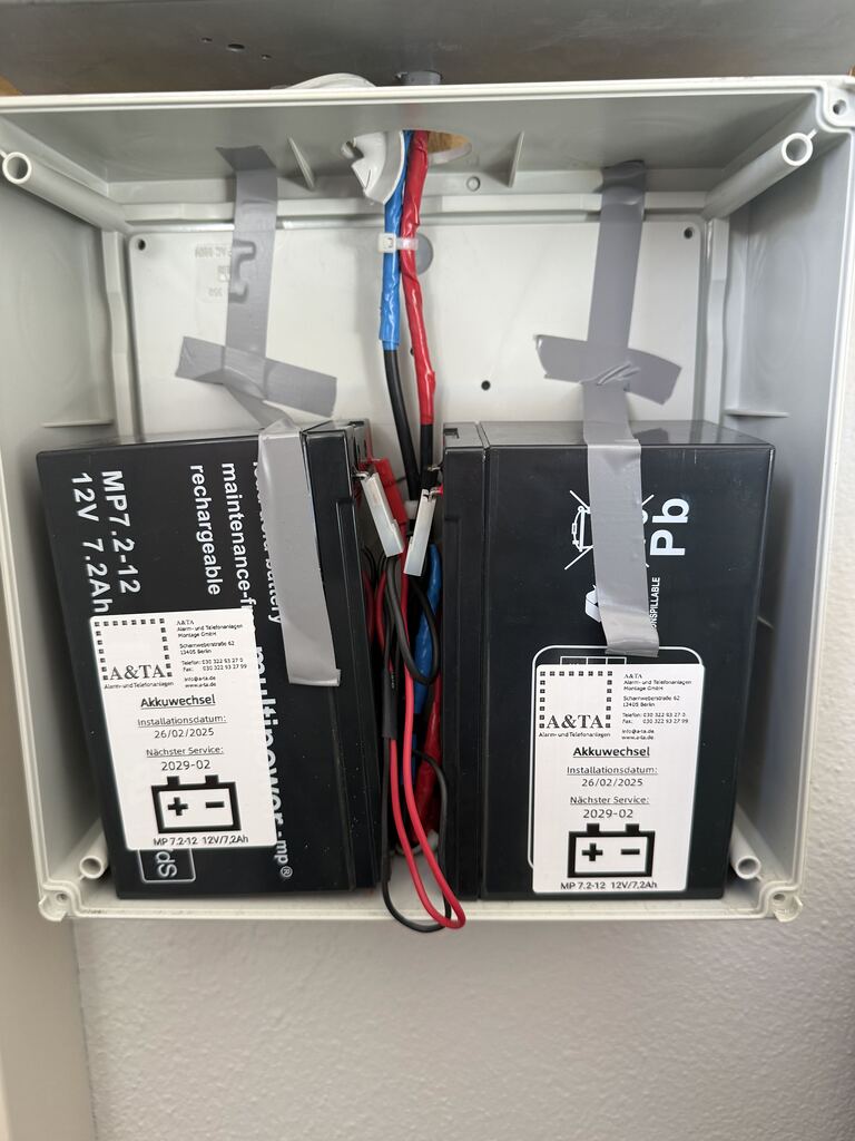 Zwei Akkus im geöffneten Gehäuse einer Sicherheitsanlage mit A&TA-Aufklebern zum Akkuwechsel und nächsten Service.